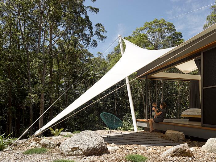 Toldo forma uma varanda à frente de um dos quartos, onde a mãe segura o bebê. Portas e teto abertos na Tent House